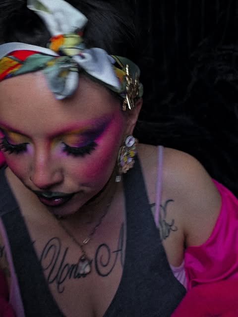 Vivid pink and purple eyeshadow with a yellow inner-eye accent and dark glossy lips.